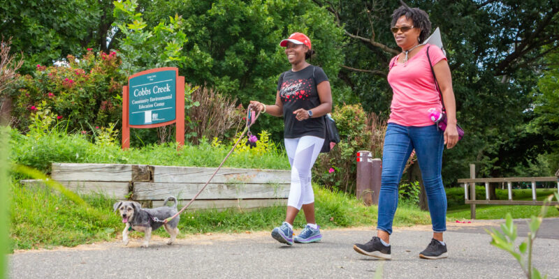 Two women walking a small dog along the Cobbs Creek Trail in Philadelphia