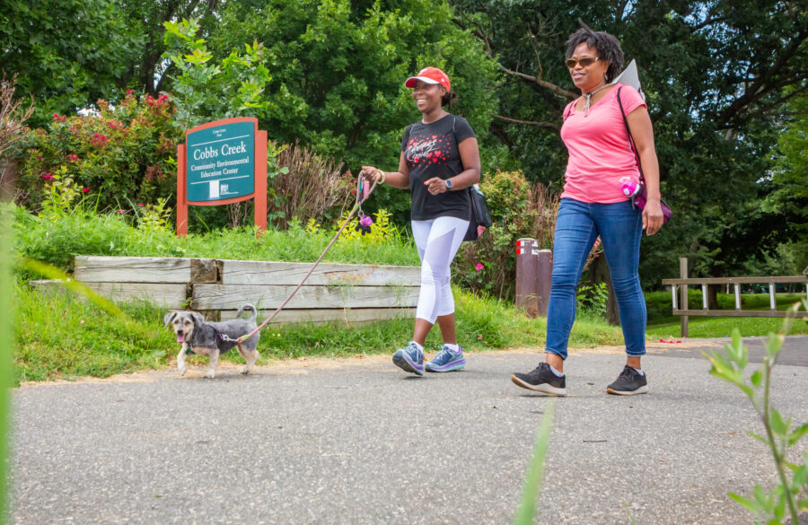 Two women walking a small dog along the Cobbs Creek Trail in Philadelphia