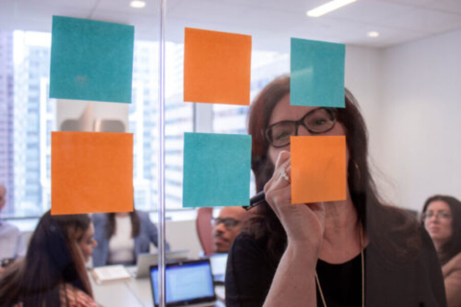 woman writing on blue and orange post-it notes aranged on a glass wall