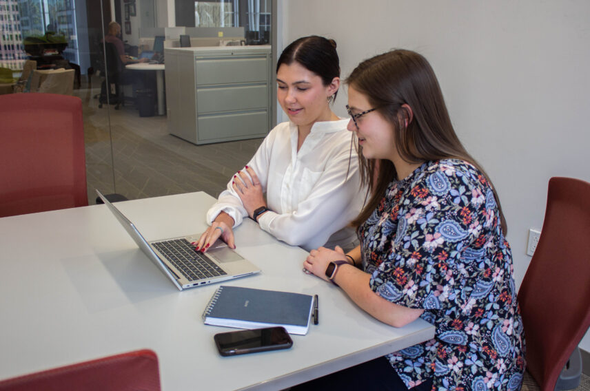 two brunette young women working on a laptop together