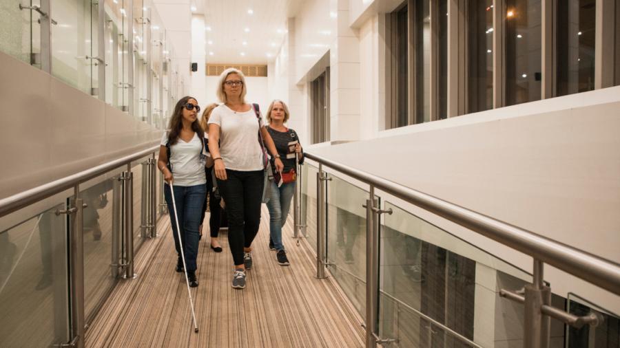 a woman with low vision using a white cane walking down a ramp with friends