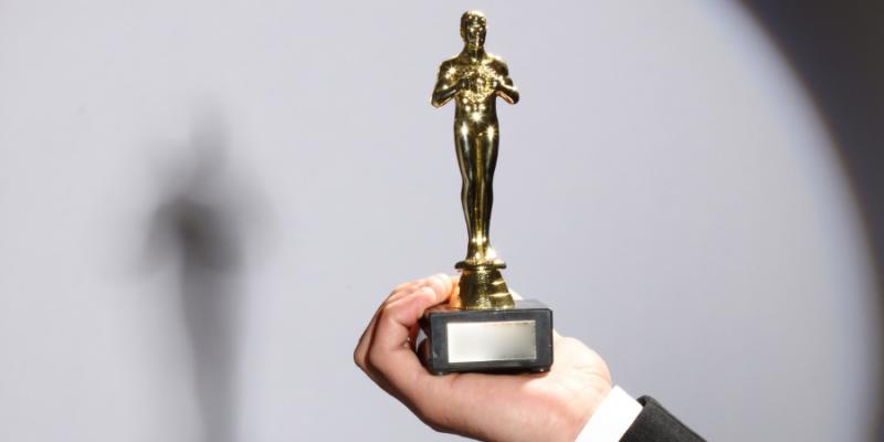 a man's hand holding up a gold Oscar statue