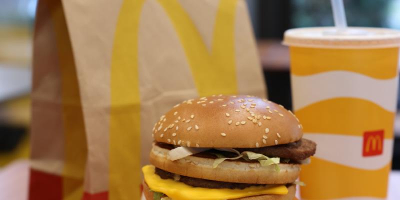 McDonald's brown paper bag behind a hamburger and a yellow and white drink cup