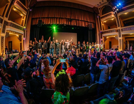 group of people on a stage holding hands with arms up infront of an applauding auidence